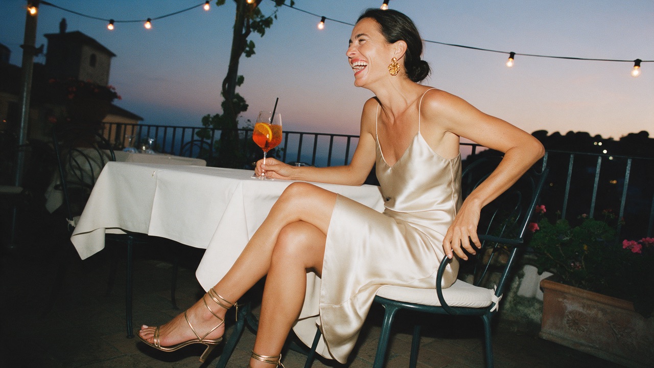 Woman in a champagne slip dress with gold earrings and strappy sandals